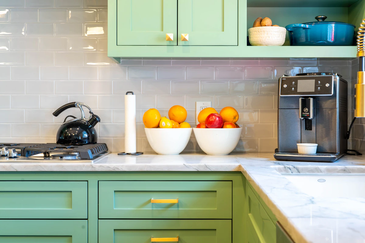 Close-up of painted green drawer fronts with brass pulls under a marble countertop